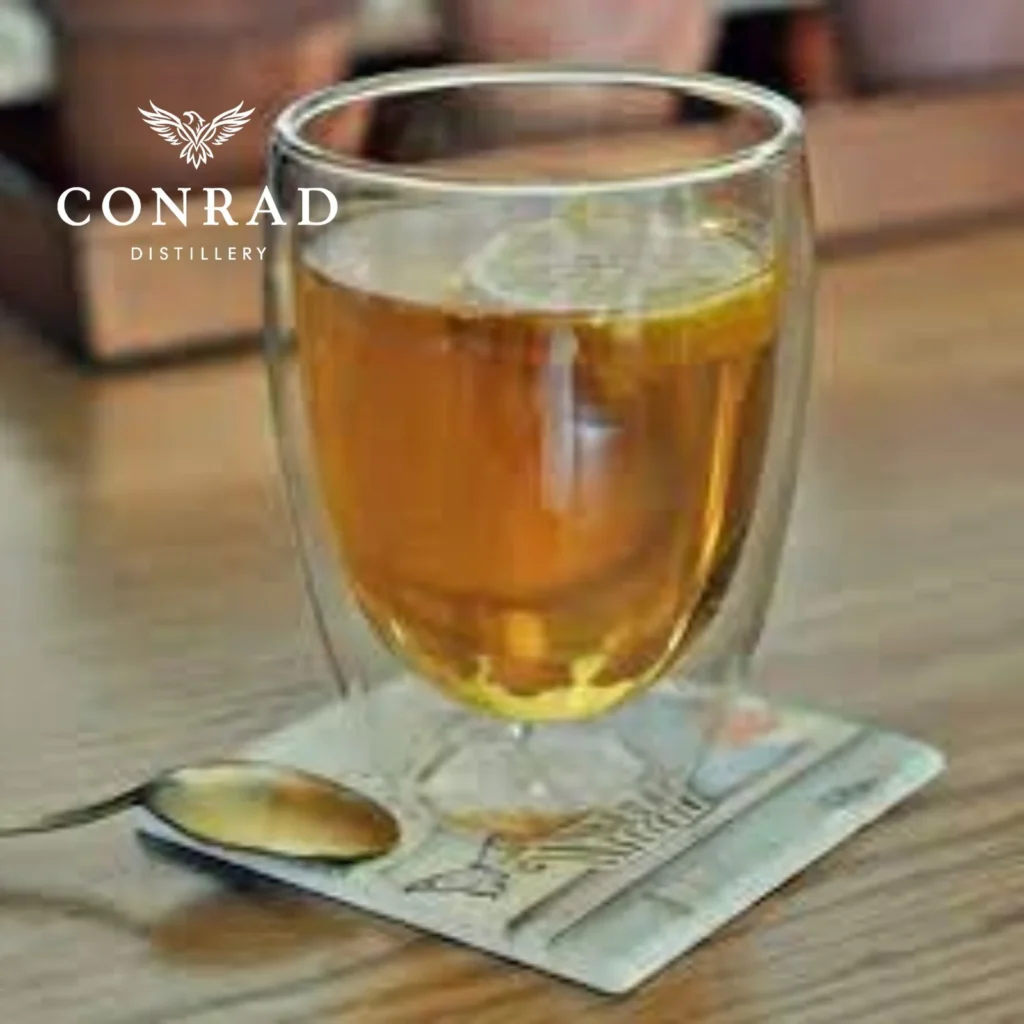 Hot Conrad G&Tea served in a double-wall glass with lemon slice on a wooden table