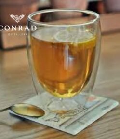 Hot Conrad G&Tea served in a double-wall glass with lemon slice on a wooden table
