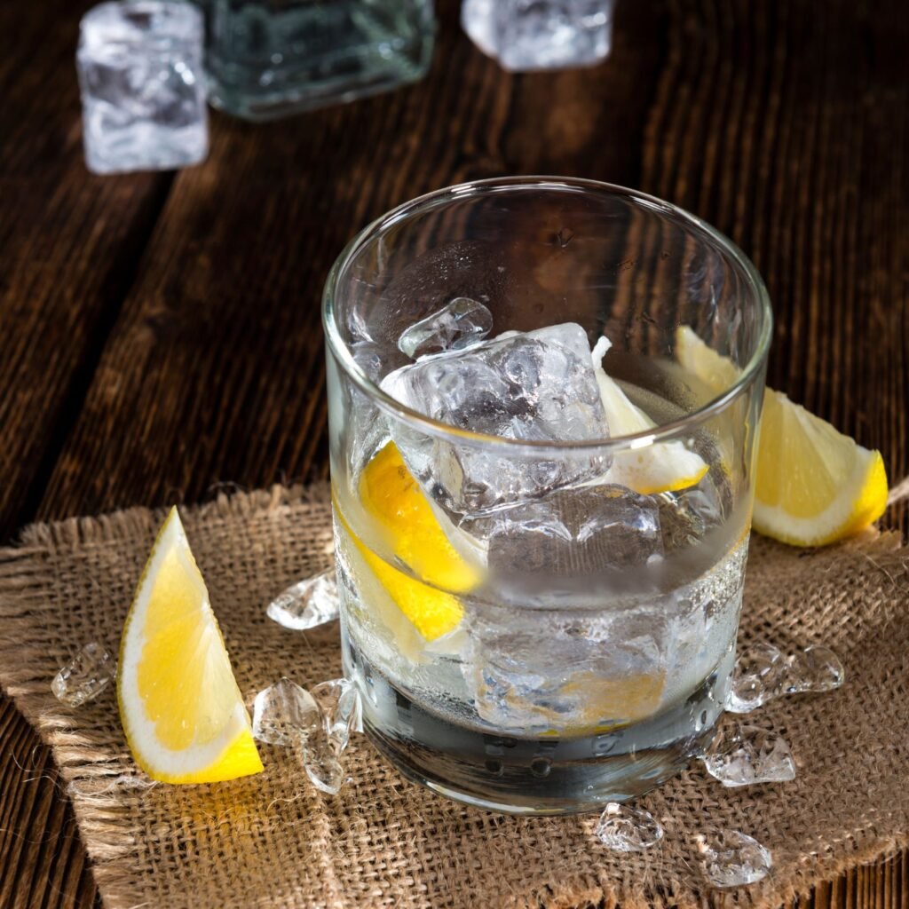 “Glass of Conrad Sidecar Navy Strength Gin on ice with fresh lemon wedges on a rustic wooden table”