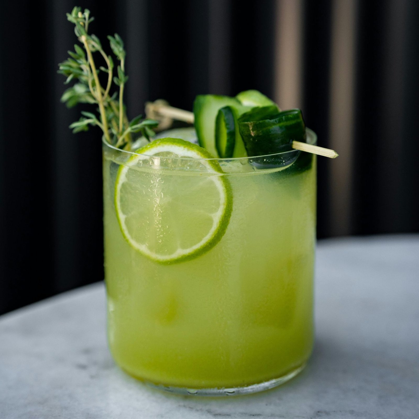 Bright green gin cocktail garnished with cucumber ribbons, lime slice and fresh thyme sprig