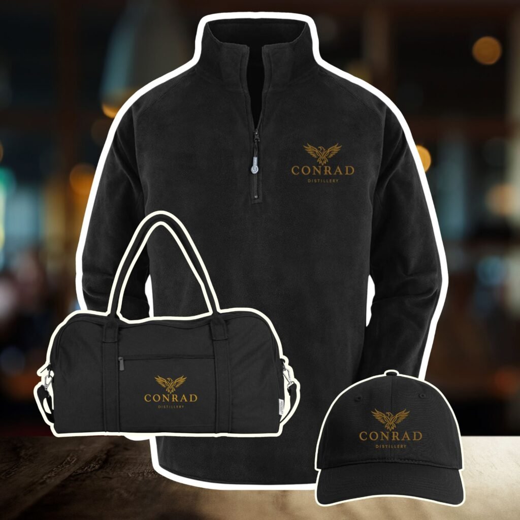 “Conrad Distillery branded black fleece, duffel bag and cap with gold logo displayed together”
