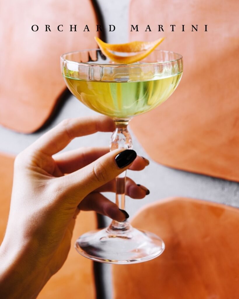 Orchard Martini cocktail made with Conrad Vodka served in a coupe glass with an orange twist garnish.