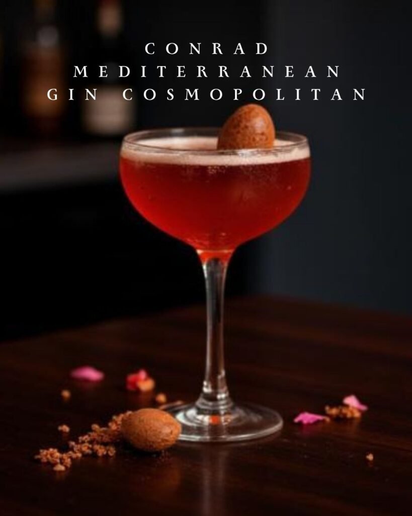 Mediterranean Gin Cosmopolitan cocktail in coupe glass with smooth foam top and chocolate egg garnish on a dark setting.