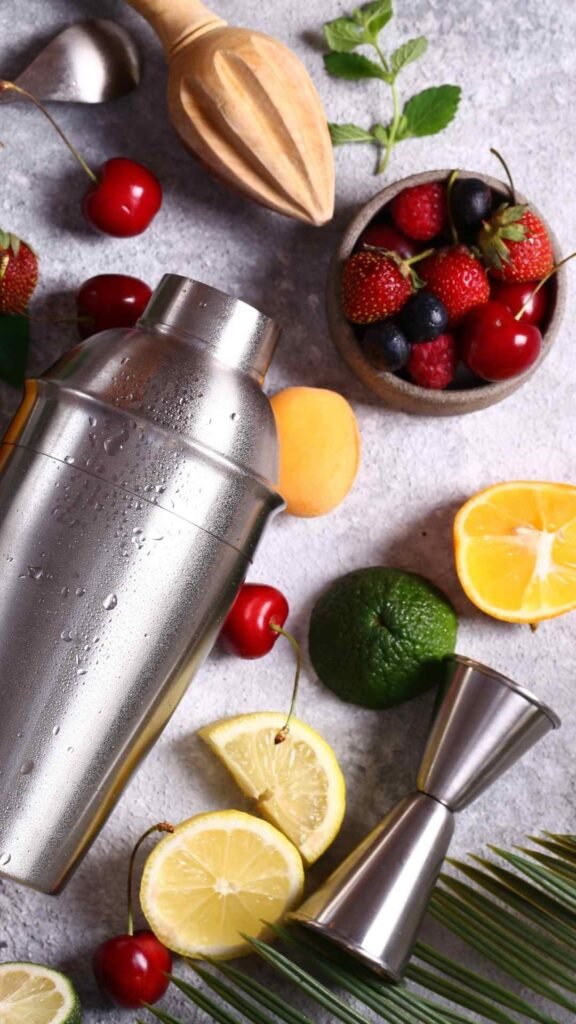Cocktail shaker surrounded by fresh citrus, berries, herbs and bar tools used for crafting premium cocktails and mixed drinks.