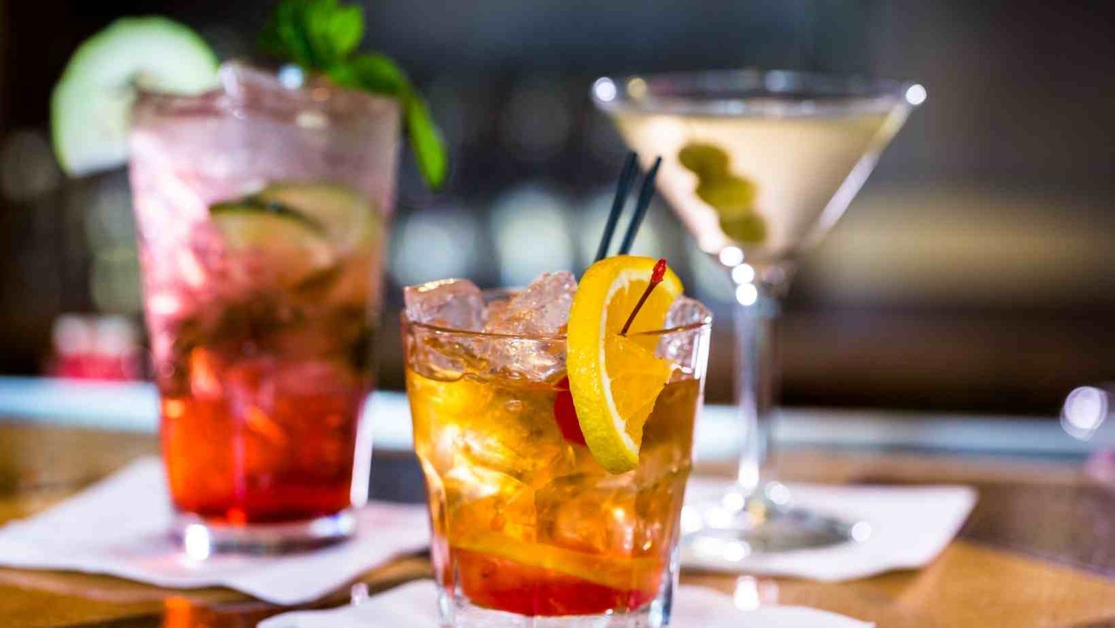 Three handcrafted vodka cocktails featuring citrus, cucumber and martini garnishes displayed on a bar with a softly blurred background.